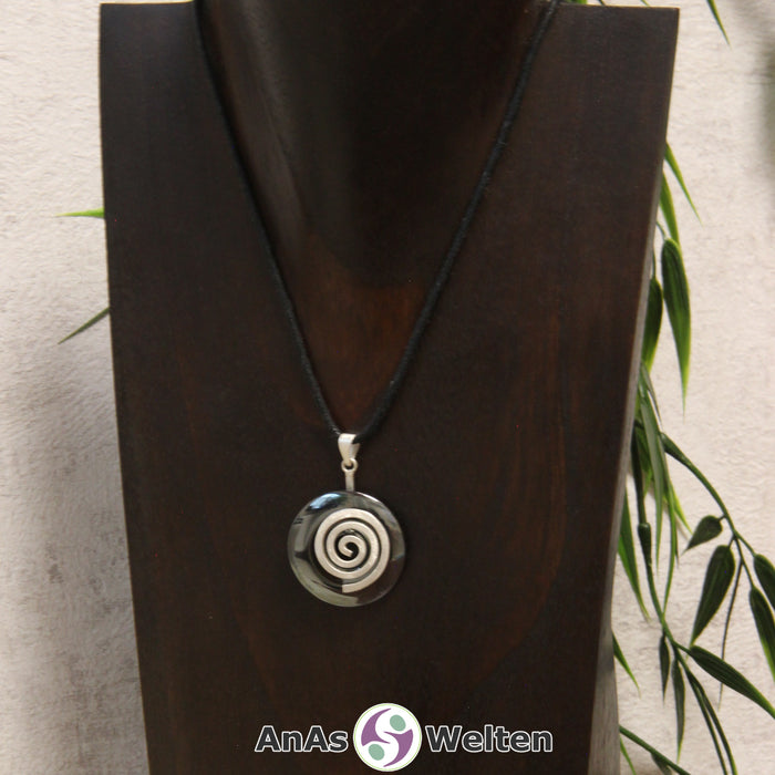 Ein Hämatit Donut an einem Donut-Halter Spirale, der mit einem gewachsten Baumwollband um eine dunkle Büste hängt.