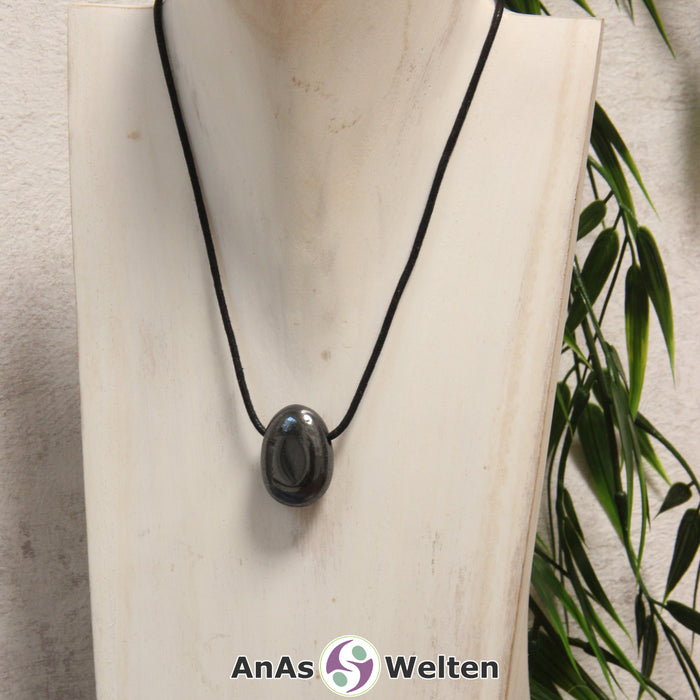 Ein silbergrauer Hämatit gebohrter Trommelstein an einem schwarzen Baumwollband, der um eine helle Büste gehängt wurde.