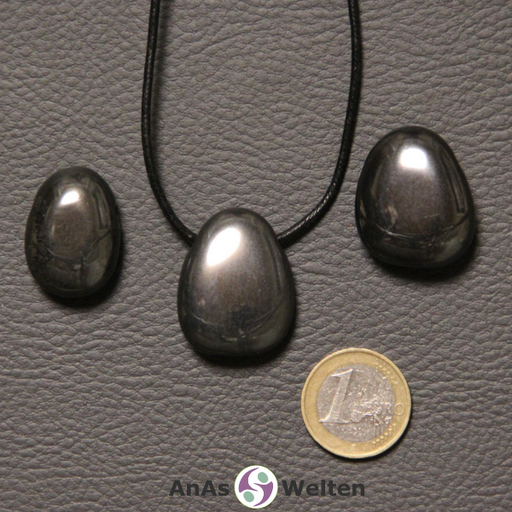 Drei silbergraue Hämatit gebohrte Trommelsteine nebeneinander. Einer befindet sich an einem schwarzen gewachsten Baumwollband.