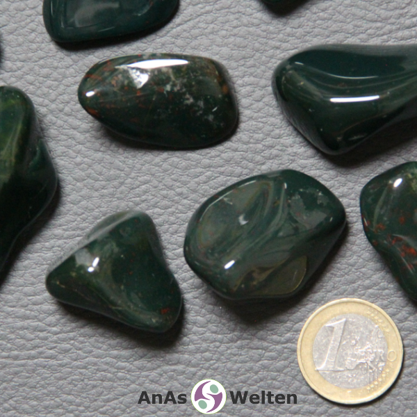 Das Bild zeigt einen Heliotrop Trommelstein anhand von mehreren Beispielsteinen. Die Edelsteine sind dunkelgrün mit gelegentlichen roten Sprenkeln.