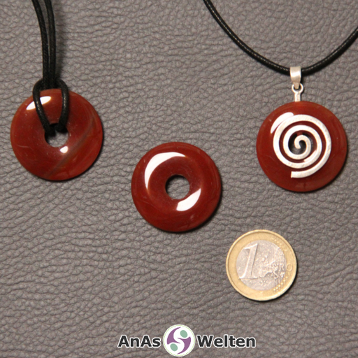 Drei Karneol Donuts nebeneinander. Einer an einem Baumwollband, ein anderer an einem Donut-Halter mit Baumwollband.