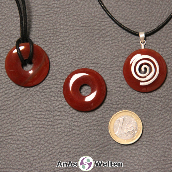 Drei Karneol Donuts nebeneinander. Einer an einem Baumwollband, ein anderer an einem Donut-Halter mit Baumwollband.