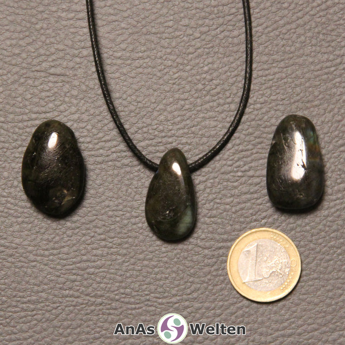 Drei blauschimmernde Labradorit gebohrte Trommelsteine nebeneinander. Einer befindet sich an einem schwarzen gewachsten Baumwollband.