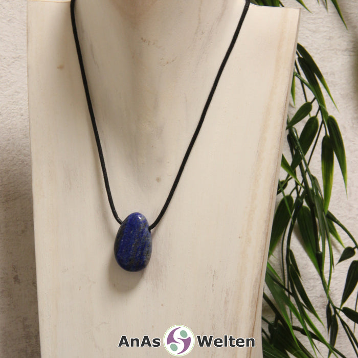 Ein blauer Lapislazuli gebohrter Trommelstein an einem schwarzen Baumwollband, der um eine helle Büste gehängt wurde.