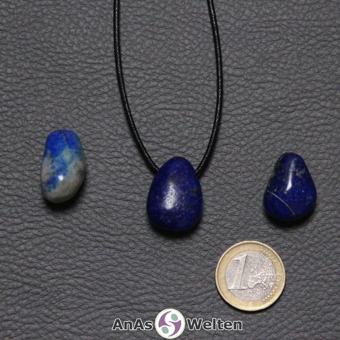 Drei blaue Lapislazuli gebohrte Trommelsteine nebeneinander. Einer befindet sich an einem schwarzen gewachsten Baumwollband.