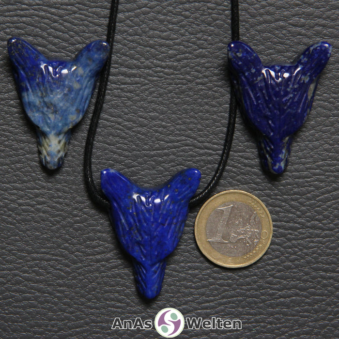 Drei Lapislazuli Wolf Anhänger nebeneinander. Einer befindet sich an einem schwarzen Baumwollband.