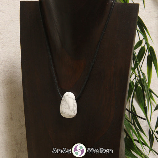 Ein gebohrter Magnesit Trommelstein an einem Baumwollband. Der Stein sieht Marmor sehr ähnlich. Er hat die typische Weiße Farbe und ist von grauen Linien durchzogen.