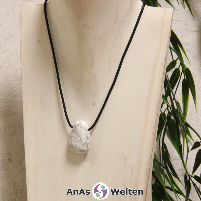 Ein weißer Magnesit gebohrter Trommelstein an einem schwarzen Baumwollband, der um eine helle Büste gehängt wurde.