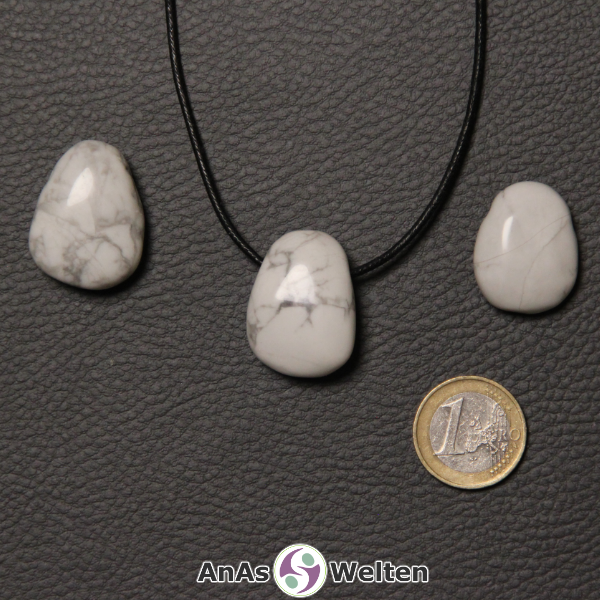 Drei weiße Magnesit gebohrte Trommelsteine nebeneinander. Einer befindet sich an einem schwarzen gewachsten Baumwollband.