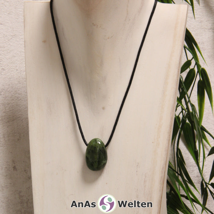 Ein grüner Nephrit Jade gebohrter Trommelstein an einem schwarzen Baumwollband, der um eine helle Büste gehängt wurde.