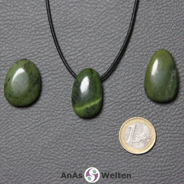 Drei grüne Nephrit Jade gebohrte Trommelsteine nebeneinander. Einer befindet sich an einem schwarzen gewachsten Baumwollband.