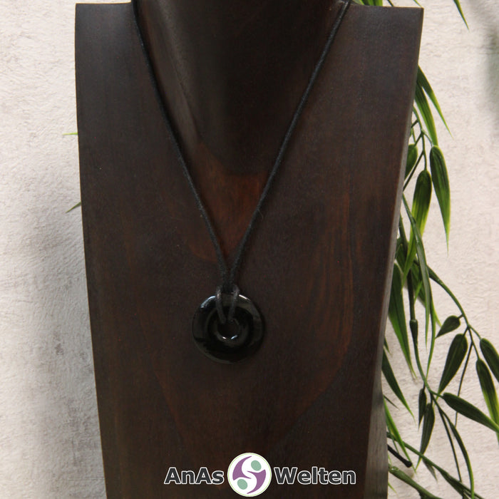 Ein Onyx Donut als Kette an einem schwarzen gewachsten Baumwollband um eine dunkle Büste.