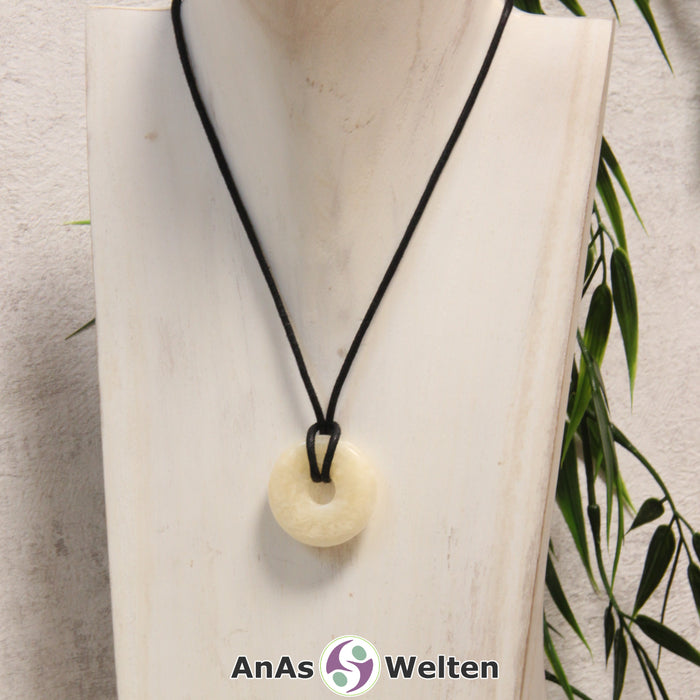 Ein Orangencalcit Donut als Kette an einem schwarzen gewachsten Baumwollband um eine helle Büste.