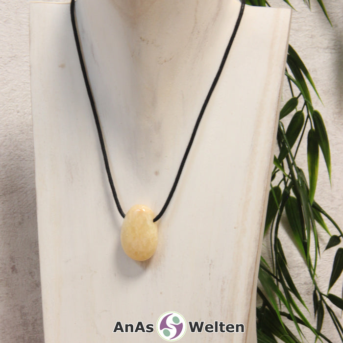 Ein gelber Orangencalcit gebohrter Trommelstein an einem schwarzen Baumwollband, der um eine helle Büste gehängt wurde.