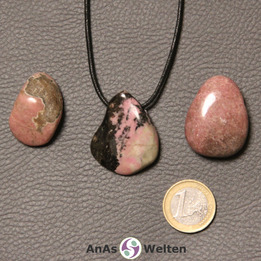 Drei rosa-schwarze Rhodonit gebohrte Trommelsteine nebeneinander. Einer befindet sich an einem schwarzen gewachsten Baumwollband.