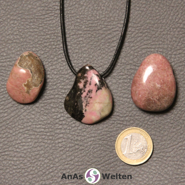 Drei rosa-schwarze Rhodonit gebohrte Trommelsteine nebeneinander. Einer befindet sich an einem schwarzen gewachsten Baumwollband.