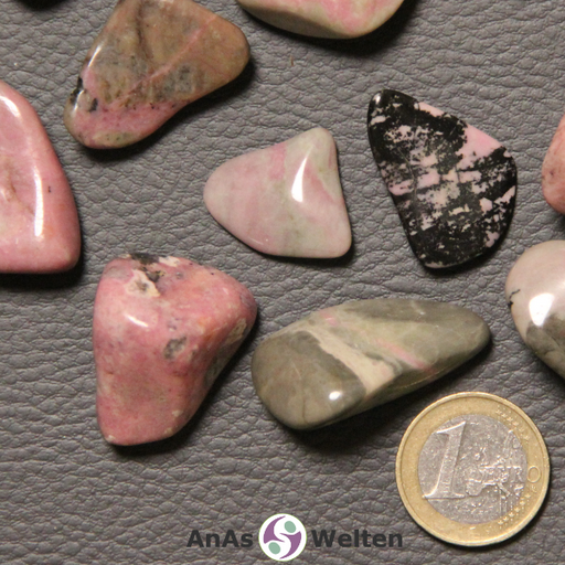 Das Bild zeigt einen Rhodonit Trommelstein anhand mehrerer Beispielsteine. Die Edelsteine sehen teilweise sehr verschieden aus, haben aber fast alle einen lachsfarbenen Grundton. Viele haben außerdem einen gewissen Beigeanteil, während einer hauptsächlich graubraun ist und ein anderer lachs und schwarz.