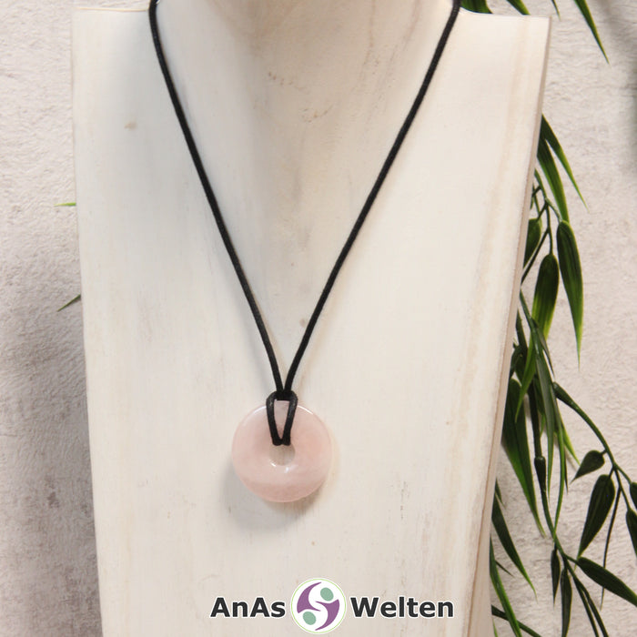 Ein Rosenquarz Donut als Kette an einem schwarzen gewachsten Baumwollband um eine helle Büste.