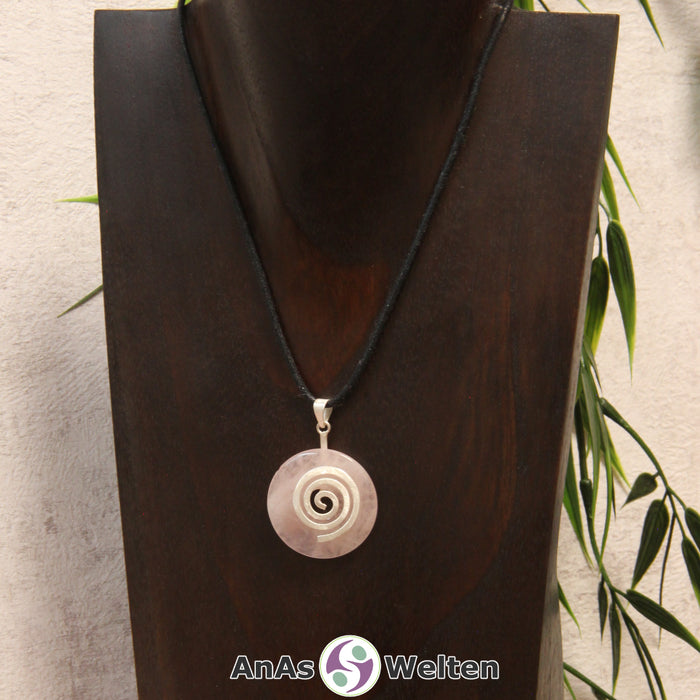 Ein Rosenquarz Donut an einem Donut-Halter Spirale, der mit einem gewachsten Baumwollband um eine dunkle Büste hängt.