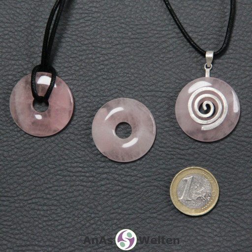 Drei Rosenquarz Donuts nebeneinander. Einer an einem Baumwollband, ein anderer an einem Donut-Halter mit Baumwollband.