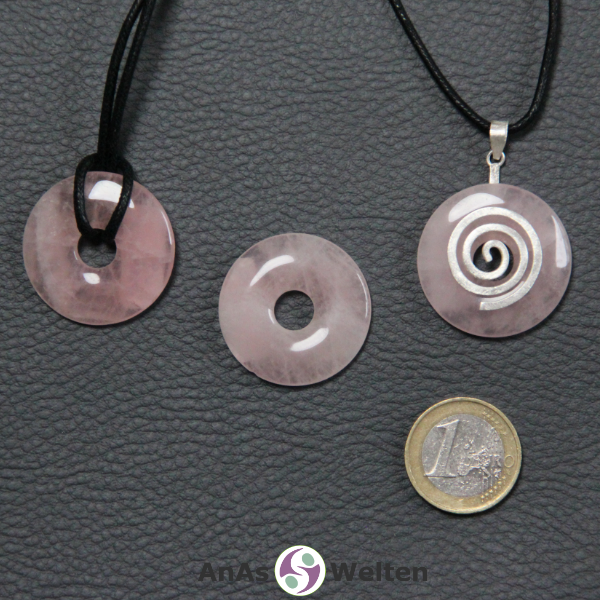 Drei Rosenquarz Donuts nebeneinander. Einer an einem Baumwollband, ein anderer an einem Donut-Halter mit Baumwollband.