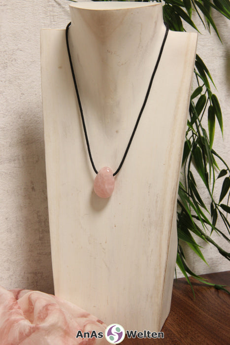 Ein rosa Rosenquarz gebohrter Trommelstein an einem schwarzen Baumwollband, der um eine helle Büste gehängt wurde.