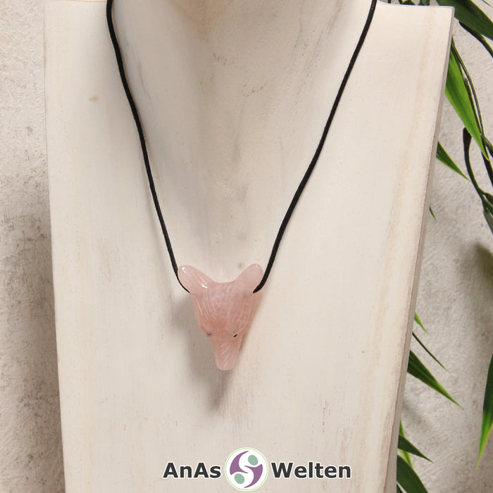 Ein Rosenquarz Wolf Anhänger an einem schwarzen Baumwollband, der um eine dunkle Büste gehängt wurde.