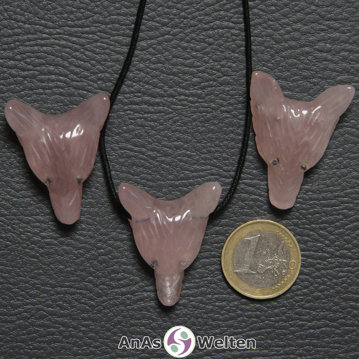 Drei Rosenquarz Wolf Anhänger nebeneinander. Einer befindet sich an einem schwarzen Baumwollband.