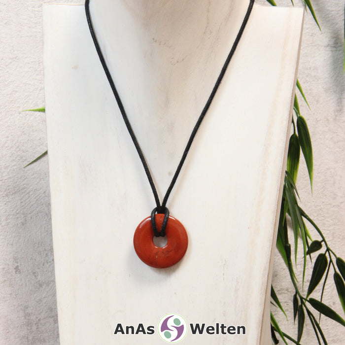 Ein Roter Jaspis Donut als Kette an einem schwarzen gewachsten Baumwollband um eine helle Büste.