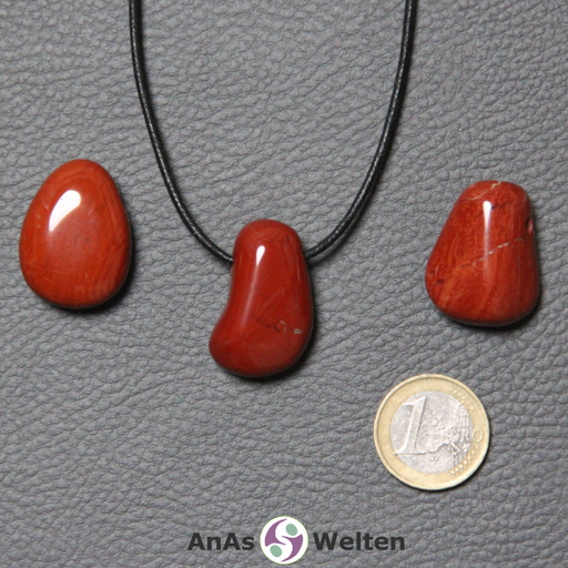 Drei Roter Jaspis gebohrte Trommelsteine nebeneinander. Einer befindet sich an einem schwarzen gewachsten Baumwollband.