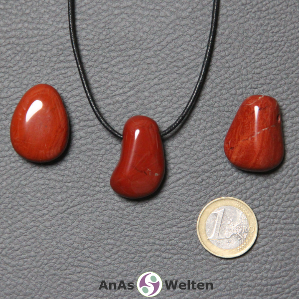Drei Roter Jaspis gebohrte Trommelsteine nebeneinander. Einer befindet sich an einem schwarzen gewachsten Baumwollband.