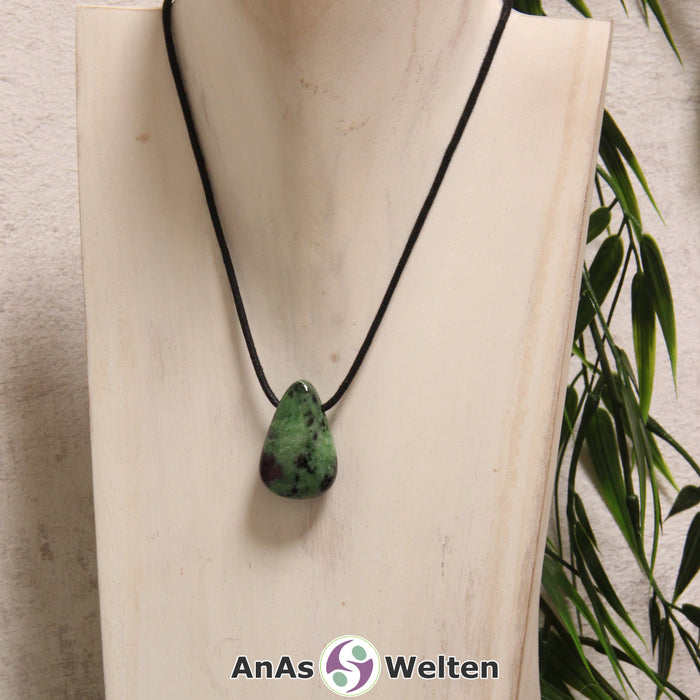 Ein rot-grüner Rubin Zoisit gebohrter Trommelstein an einem schwarzen Baumwollband, der um eine helle Büste gehängt wurde.