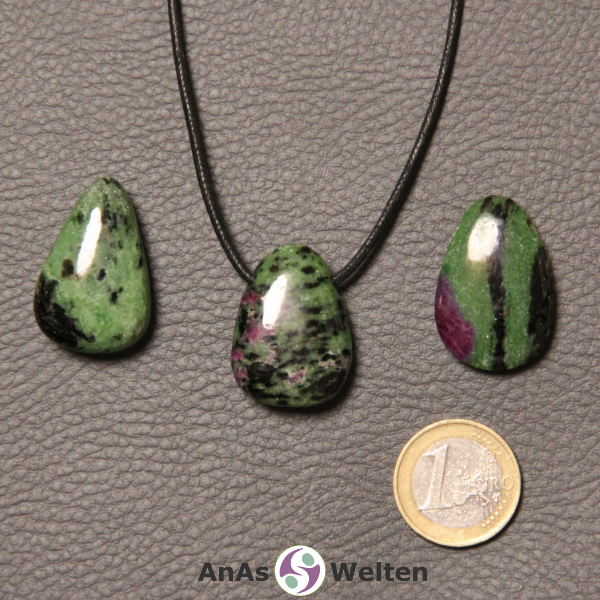 Drei rot-grüne Rubin Zoisit gebohrte Trommelsteine nebeneinander. Einer befindet sich an einem schwarzen gewachsten Baumwollband.