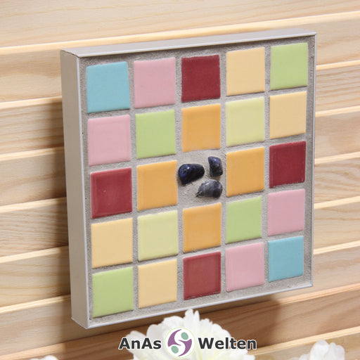 Das Bild zeigt ein Sator Quadrat Mosaik in Pastellfarben mit einem Aluminiumrahmen. Dort, wo im Sator Quadrat die Buchstaben stehen, sind hier viereckige Fliesen zu sehen, die je eine Farbe pro unterschiedlichen Buchstaben haben. In der Mitte, wo normalerweise das N steht, sind vier Sodalithe in den Fugenmörtel eingesetzt.