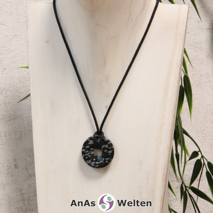 Ein Schneeflocken-Obsidian Donut als Kette an einem schwarzen gewachsten Baumwollband um eine helle Büste.