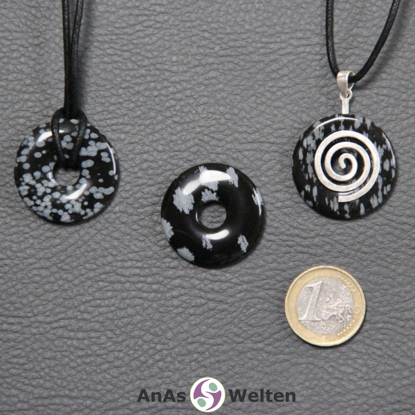 Drei Schneeflocken-Obsidian Donuts nebeneinander. Einer an einem Baumwollband, ein anderer an einem Donut-Halter mit Baumwollband.