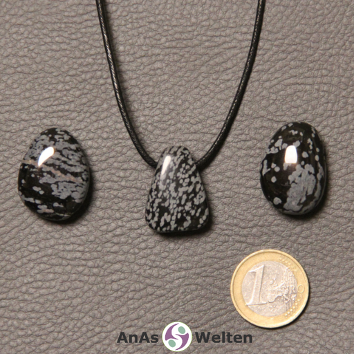 Drei schwarz-weiße Schneeflocken-Obsidian gebohrte Trommelsteine nebeneinander. Einer befindet sich an einem schwarzen gewachsten Baumwollband.