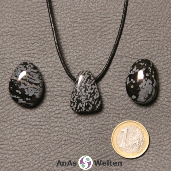 Drei schwarz-weiße Schneeflocken-Obsidian gebohrte Trommelsteine nebeneinander. Einer befindet sich an einem schwarzen gewachsten Baumwollband.