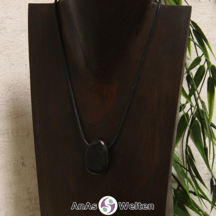 Ein schwarzer Schungit gebohrter Trommelstein an einem schwarzen Baumwollband, der um eine dunkle Büste gehängt wurde.