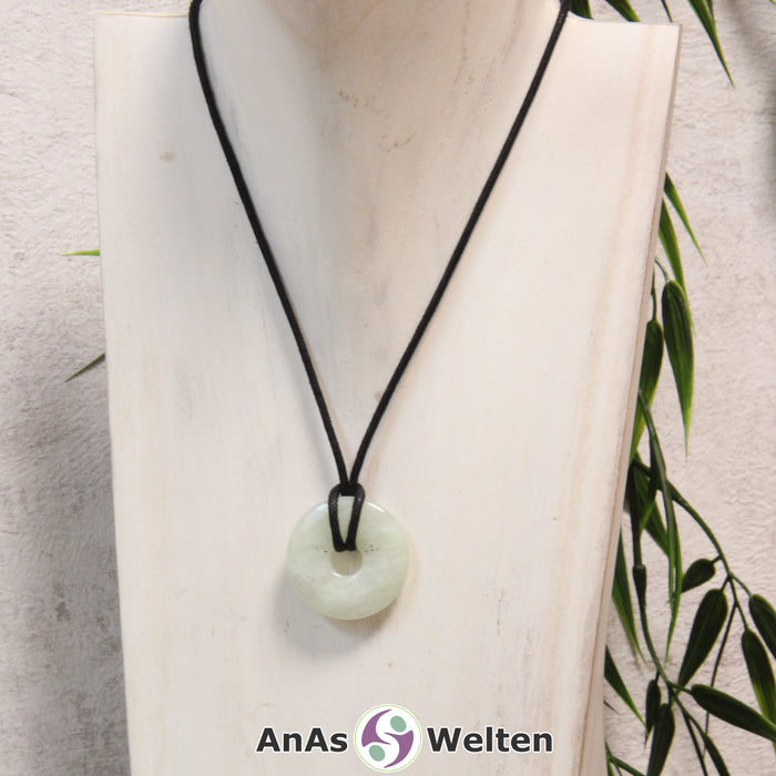 Ein Serpentin Donut als Kette an einem schwarzen gewachsten Baumwollband um eine helle Büste.