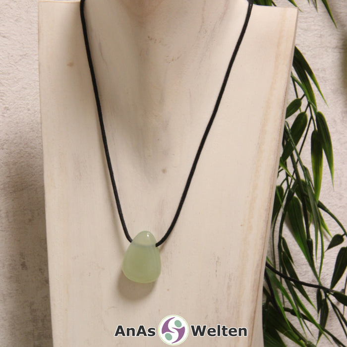 Ein grüner Serpentin gebohrter Trommelstein an einem schwarzen Baumwollband, der um eine helle Büste gehängt wurde.