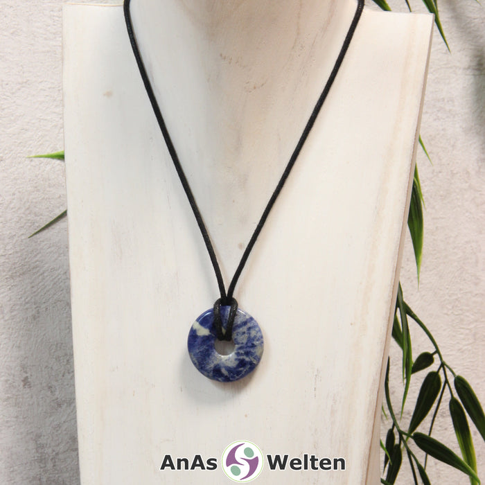 Ein Sodalith Donut als Kette an einem schwarzen gewachsten Baumwollband um eine helle Büste.