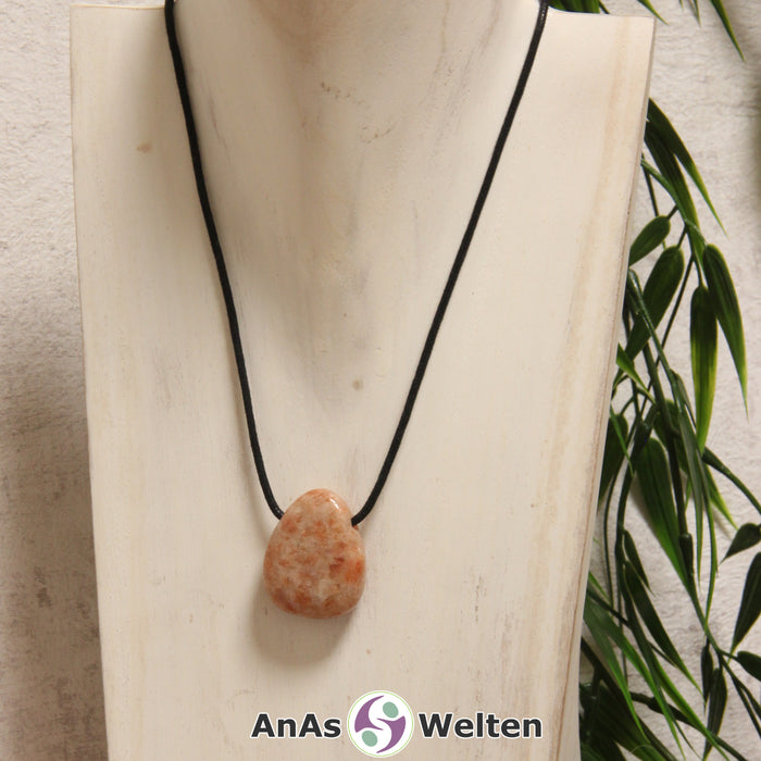 Ein rot-gelb-brauner Sonnenstein gebohrter Trommelstein an einem schwarzen Baumwollband, der um eine helle Büste gehängt wurde.