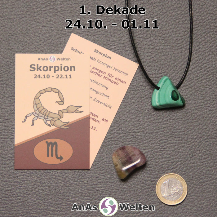 Die Sternzeichenkarte und je ein beispielhafter gebohrter Malachit Trommelstein am Band und ein Fluorit Trommelstein der 1. Dekade liegen nebeneinander.