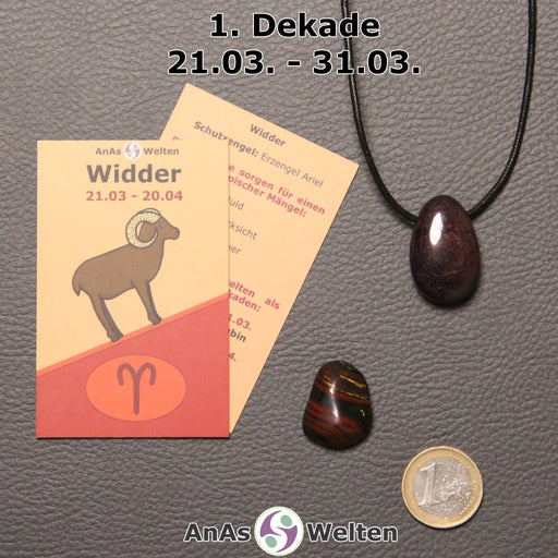 Die Sternzeichenkarte und je ein beispielhafter gebohrter Granat Trommelstein am Band und ein Tigereisen Trommelstein der 1. Dekade liegen nebeneinander.