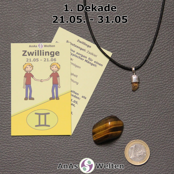 Die Sternzeichenkarte und je ein beispielhafter Goldtopas mit Öse am Band und ein Tigerauge Trommelstein der 1. Dekade liegen nebeneinander.
