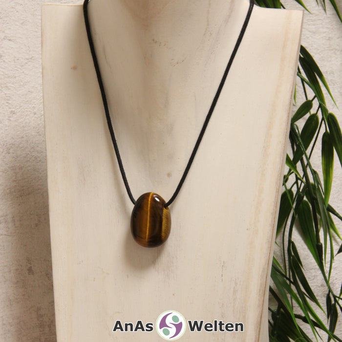 Ein braunschimmernder Tigerauge gebohrter Trommelstein an einem schwarzen Baumwollband, der um eine helle Büste gehängt wurde.