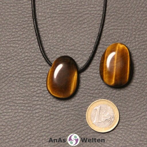 Zwei braunschimmernde Tigerauge gebohrte Trommelsteine nebeneinander. Einer befindet sich an einem schwarzen gewachsten Baumwollband.