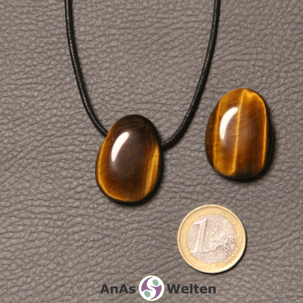 Zwei braunschimmernde Tigerauge gebohrte Trommelsteine nebeneinander. Einer befindet sich an einem schwarzen gewachsten Baumwollband.