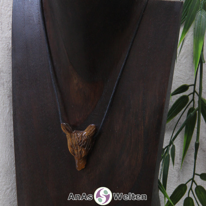 Ein Tigerauge Wolf Anhänger an einem schwarzen Baumwollband, der um eine dunkle Büste gehängt wurde.